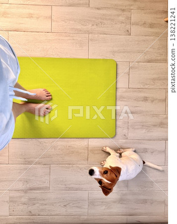 A girl stands on a lemon-colored yoga mat with her pet, a Jack Russell Terrier A girl stands on a lemon-colored yoga mat with her pet, a Jack Russell Terrier 138221241