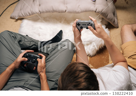 Close-up of two male friends gaming together at home, enjoying console video games during leisure time, having fun and unwinding while sharing entertaining moments and screen time. Close-up of two male friends gaming together at home, enjoying console video games during leisure time, having fun and unwinding while sharing entertaining moments and screen time. 138222410
