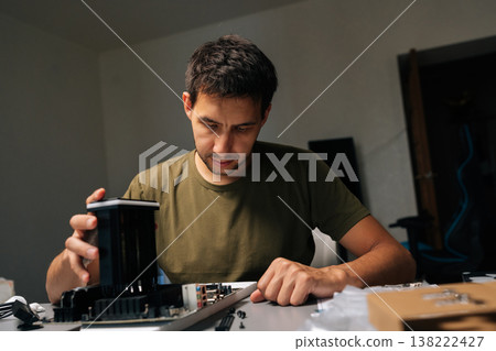 Portrait of computer technician male installing CPU cooler onto motherboard, performing maintenance and repair work on desktop computer in dark workshop. Concept of computer hardware, repairing. 138222427