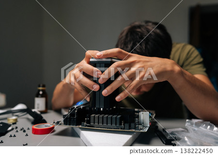 Computer technician carefully installing CPU cooler onto motherboard, performing maintenance or repair work in dimly lit workshop, surrounded by various computer components. Computer technician carefully installing CPU cooler onto motherboard, performing maintenance or repair work in dimly lit workshop, surrounded by various computer components. 138222450