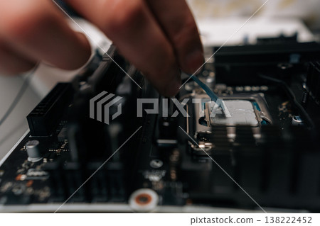 Close-up hands of unrecognizable technician applying thermal paste on computer processor, spreading precise layer for efficient cooling and improved performance during hardware maintenance. 138222452