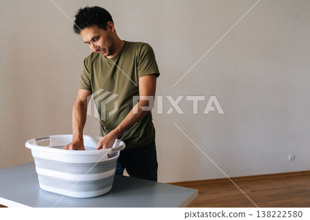 Portrait of handsome focused young man washing clothes by hand in plastic basin, wringing out water performing domestic task. Concept of housework, housekeeping and household. 138222580