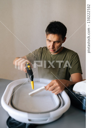 Homemaker male cleaning humidifier filter using steam cleaner, submerging filter in water basin for sanitizing, ensuring optimal indoor air quality and respiratory health. Concept of healthy lifestyle Homemaker male cleaning humidifier filter using steam cleaner, submerging filter in water basin for sanitizing, ensuring optimal indoor air quality and respiratory health. Concept of healthy lifestyle 138222582