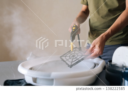 Cropped shot of housewife using steam cleaner to clean air humidifier filter in basin at home, ensuring regular maintenance for maintaining healthy indoor air quality. Concept of household cleanliness Cropped shot of housewife using steam cleaner to clean air humidifier filter in basin at home, ensuring regular maintenance for maintaining healthy indoor air quality. Concept of household cleanliness 138222585
