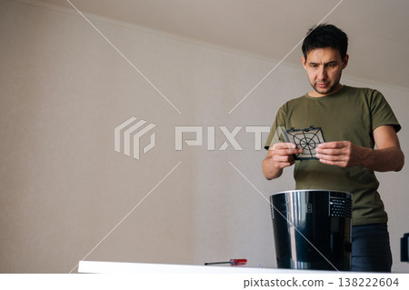 Focused technician male examining humidifier filter, cleaning and replacing component, ensuring optimal indoor air quality and maintaining healthy home environment. Concept of household cleanliness. 138222604