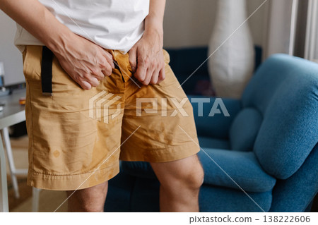 Cropped shot of unhealthy young man grappling with urinary incontinence, anxiously clutching wet pants as navigates discomfort and embarrassment of situation. Concept of healthy lifestyle. Cropped shot of unhealthy young man grappling with urinary incontinence, anxiously clutching wet pants as navigates discomfort and embarrassment of situation. Concept of healthy lifestyle. 138222606
