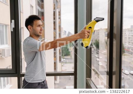 Side view of cleaning service employee using cordless vacuum cleaner to wash windows in high-rise building, ensuring streak-free shine and maintaining clear view. Concept of hygiene, cleanliness Side view of cleaning service employee using cordless vacuum cleaner to wash windows in high-rise building, ensuring streak-free shine and maintaining clear view. Concept of hygiene, cleanliness 138222617