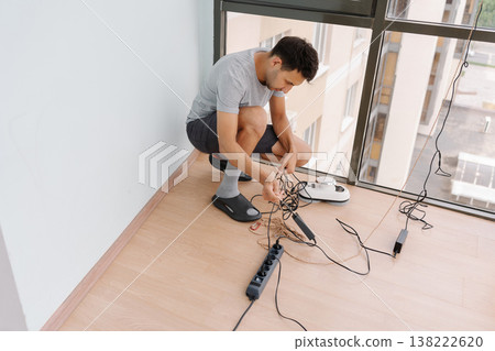 Window cleaner male untangling cables and preparing automatic robot for efficiently cleaning windows of high-rise building, showcasing modern technology and professional maintenance skills 138222620
