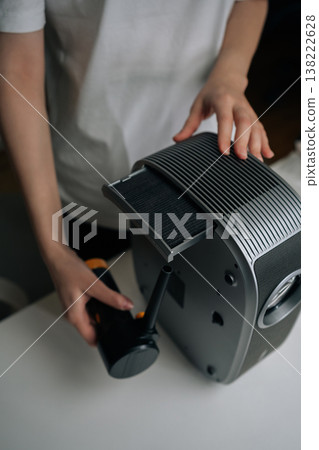 Close-up vertical cropped shot of person cleaning home cinema projector with air blower, providing regular maintenance for electronic device performance and longevity, keeping technology efficient. Close-up vertical cropped shot of person cleaning home cinema projector with air blower, providing regular maintenance for electronic device performance and longevity, keeping technology efficient. 138222628