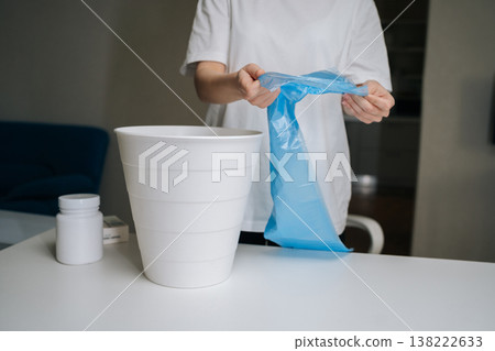 Close-up cropped shot of person preparing small bin with blue plastic garbage bag on white table, getting ready to dispose of medication, symbolizing ending addiction, recovery, fresh start. 138222633