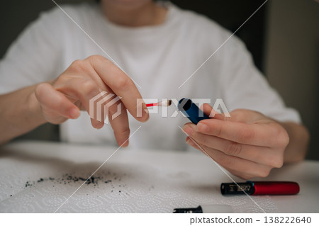 Woman cleaning electronic cigarette mouthpiece with cotton swab, removing residue for hygiene and maintenance in focused, close-up domestic self-care routine. Woman cleaning electronic cigarette mouthpiece with cotton swab, removing residue for hygiene and maintenance in focused, close-up domestic self-care routine. 138222640