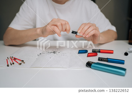 Person hands performing maintenance service on heated tobacco device, cleaning electronic cigarette with cotton swab and keeping vape device in proper condition, close-up cropped shot. Person hands performing maintenance service on heated tobacco device, cleaning electronic cigarette with cotton swab and keeping vape device in proper condition, close-up cropped shot. 138222652