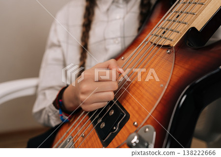 Close-up hand of unrecognizable preteen girl holding electric bass guitar and smiling, happily learning creating music, enjoying her musical hobby and development. Close-up hand of unrecognizable preteen girl holding electric bass guitar and smiling, happily learning creating music, enjoying her musical hobby and development. 138222666