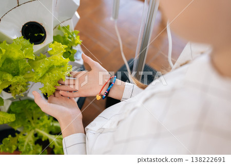 Cropped shot of child girl caring for plants in modern indoor vertical hydroponic garden, learning about sustainable home farming and urban agriculture. Concept of home gardening.. Cropped shot of child girl caring for plants in modern indoor vertical hydroponic garden, learning about sustainable home farming and urban agriculture. Concept of home gardening.. 138222691