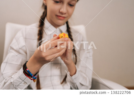 Happy young girl enjoying simple childhood play, finding focus and relaxation while interacting with a yellow rubber duck toy, fostering sensory development and playful engagement. 138222706