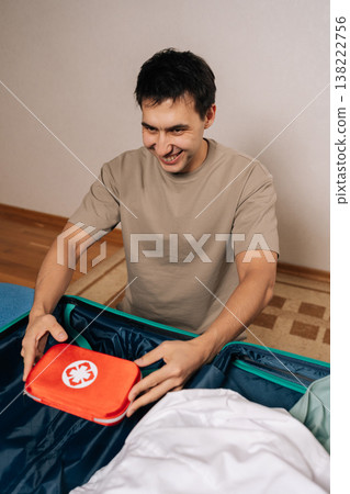 Vertical portrait of cheerful traveler packing essential travel medicine bag into a suitcase, prioritizing health and safety during a journey, preparing for potential emergencies away from home. 138222756