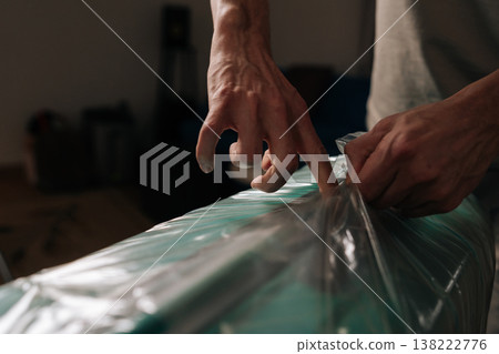 Person is unwrapping a turquoise suitcase with transparent plastic film at home, protecting luggage from damage and theft, ensuring safe travel for a journey, preparing for an upcoming vacation. Person is unwrapping a turquoise suitcase with transparent plastic film at home, protecting luggage from damage and theft, ensuring safe travel for a journey, preparing for an upcoming vacation. 138222776