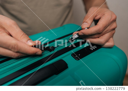 Close-up cropped shot of person securing a teal suitcase zipper and integrated combination lock, demonstrating travel readiness and protection of valuables during a holiday or relocation. Close-up cropped shot of person securing a teal suitcase zipper and integrated combination lock, demonstrating travel readiness and protection of valuables during a holiday or relocation. 138222779