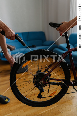 Vertical cropped shot of two friends cyclists cleaning bicycle wheel using high-pressure steam cleaner, removing stubborn dirt at home, demonstrating meticulous bicycle maintenance technique. 138222818