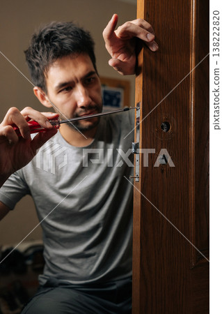 Vertical portrait of professional male fixing door lock with screwdriver, performing installation and repair work on mechanism to ensure security and functionality within house. Vertical portrait of professional male fixing door lock with screwdriver, performing installation and repair work on mechanism to ensure security and functionality within house. 138222820