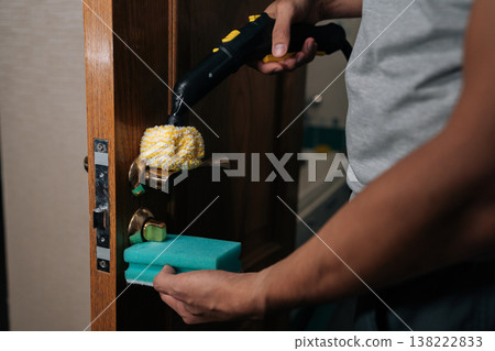 Cropped shot of unrecognizable man steam cleaning door handle for deep disinfection, killing germs and sanitizing frequently touched surfaces in home, ensuring hygiene and healthy environment. Cropped shot of unrecognizable man steam cleaning door handle for deep disinfection, killing germs and sanitizing frequently touched surfaces in home, ensuring hygiene and healthy environment. 138222833