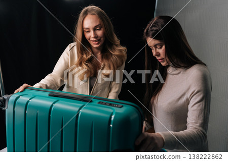 Two young women packing bright suitcase, handling travel essentials and preparing for trip, embodying travel preparation and friendship. Concept of organization and travel essentials. 138222862