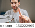 Selective focus of handsome male cleaning small desktop vanity mirror with finger, examining surface for smudges and dust, focusing on detailed household chores and personal hygiene routine. 138222905