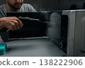 Close-up of man cleaning and sanitizing microwave oven with steam cleaner device, eliminating germs and tough stains, maintaining hygiene in kitchen at home, dark room. 138222906