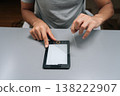 Person applying transparent screen protector film onto black digital e-reader, device for reading electronic books, protecting screen from scratches and damage. 138222907