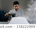 Portrait of young adult man using handheld steam cleaner to sanitize and refresh pillow through chemical-free deep cleaning, ensuring clean and hygienic sleeping space and preventing allergens. 138222909
