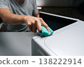 Close-up of male hand cleaning microwave oven with sponge, applying cleaner for sanitation and maintaining kitchen appliance hygiene, performing routine household chores. Concept of kitchen hygiene. 138222914
