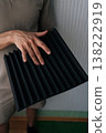 Close-up hand of handyman holding a black acoustic foam panel, exploring soundproofing materials for studio environment, noise reduction, and audio quality improvement projects. 138222919
