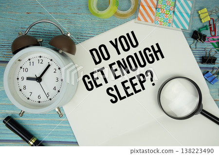 Do You Get Enough Sleep? text on a paper surrounded by office supplies, a magnifying glass, and a clock on a blue wooden surface 138223490
