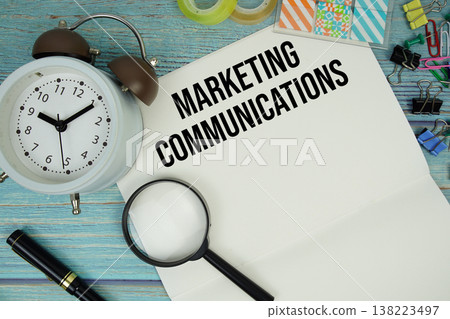 Marketing Communications text on a paper surrounded by office supplies, a magnifying glass, and a clock on a blue wooden surface Marketing Communications text on a paper surrounded by office supplies, a magnifying glass, and a clock on a blue wooden surface 138223497