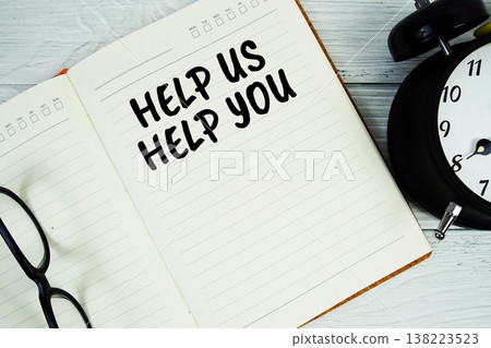 Notepad on a blue wooden table with the words "Help Us Help You" with alarm clock and eyeglasses 138223523