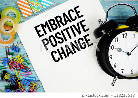Embrace Positive Change text on a paper surrounded by office supplies and a clock on a blue wooden surface Embrace Positive Change text on a paper surrounded by office supplies and a clock on a blue wooden surface 138223538