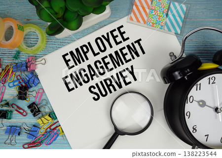 Employee Engagement Survey text on a paper surrounded by office supplies, a magnifying glass, and a clock on a blue wooden surface Employee Engagement Survey text on a paper surrounded by office supplies, a magnifying glass, and a clock on a blue wooden surface 138223544
