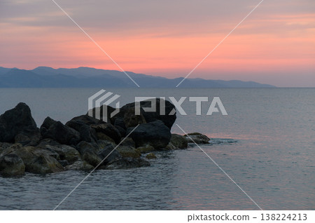 Sunset hues dance across tranquil waters by rocky shores in a serene coastal escape 138224213
