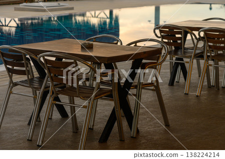 Charming outdoor dining setup by a tranquil swimming pool in the evening glow Charming outdoor dining setup by a tranquil swimming pool in the evening glow 138224214