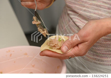 Creating delicious dumplings with care and precision in a cozy kitchen setting during a lively culinary gathering 138224251