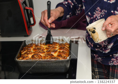 Delicious cinnamon rolls being brushed with glaze in a cozy kitchen on a chilly afternoon Delicious cinnamon rolls being brushed with glaze in a cozy kitchen on a chilly afternoon 138224337