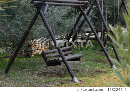 Rustic wooden swing sways gently among the olive trees in a serene garden under soft afternoon light Rustic wooden swing sways gently among the olive trees in a serene garden under soft afternoon light 138224341