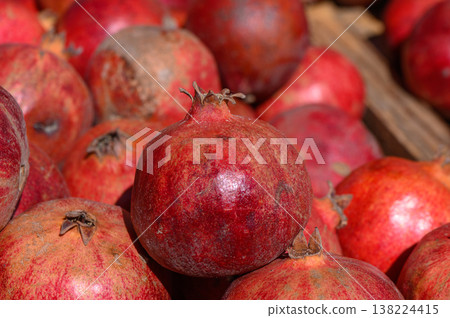 Vibrant display of ripe pomegranates basking in sunlight at a lively local market in autumn season Vibrant display of ripe pomegranates basking in sunlight at a lively local market in autumn season 138224415