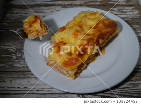 Delightful layers of cheesy chicken lasagna served on a rustic wooden table at sunset Delightful layers of cheesy chicken lasagna served on a rustic wooden table at sunset 138224452