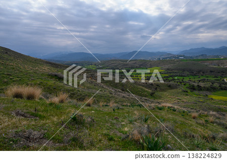 Rolling green hills under a moody sky with scattered clouds at dusk in a rural Rolling green hills under a moody sky with scattered clouds at dusk in a rural 138224829