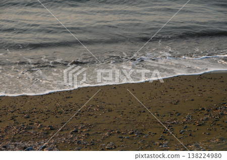 Waves gently lap against the rocky shoreline at dusk in a tranquil coastal landscape Waves gently lap against the rocky shoreline at dusk in a tranquil coastal landscape 138224980