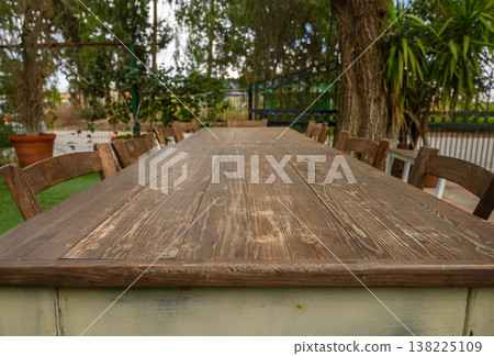 Long wooden table set for gathering in a peaceful outdoor garden during a sunny Long wooden table set for gathering in a peaceful outdoor garden during a sunny 138225109
