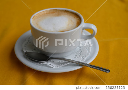 Warm cappuccino in a white cup sits elegantly on a vibrant yellow tablecloth 138225123