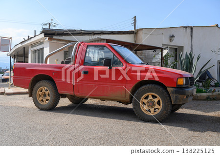 Red pickup truck parked in a dusty street near a rustic building under a clear blue sky Red pickup truck parked in a dusty street near a rustic building under a clear blue sky 138225125