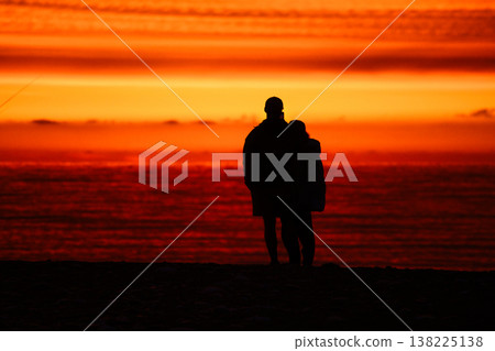 Detailed Vertical Perspective Photograph of a Silhouetted Couple Standing Close on a Pebble Beach at Dusk, Facing an Intense Crimson-Red and Orange Sea and Sunset Sky, Receding into a Wide-Open Detailed Vertical Perspective Photograph of a Silhouetted Couple Standing Close on a Pebble Beach at Dusk, Facing an Intense Crimson-Red and Orange Sea and Sunset Sky, Receding into a Wide-Open 138225138